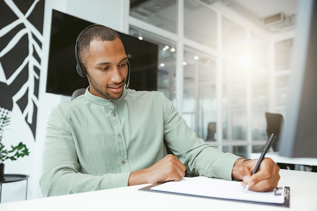 Homme d'affaires africain confiant prenant des notes tout en parlant au téléphone avec un client dans un bureau moderne