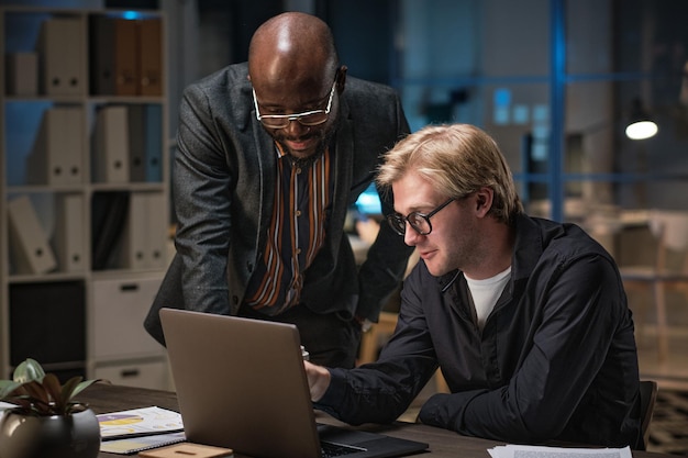 Homme d'affaires africain en costume discutant de la présentation en ligne avec son collègue pendant qu'ils utilisent un ordinateur portable au bureau