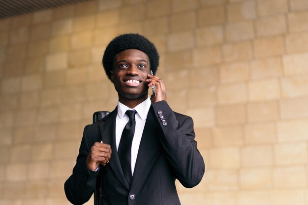 Un homme d'affaires africain en costume qui parle au téléphone et a l'air joyeux.