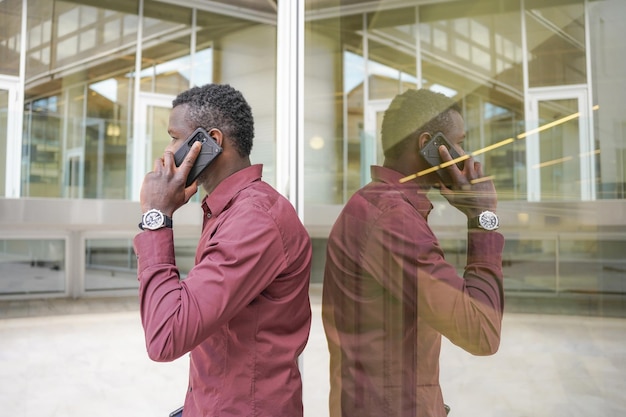 Photo homme d'affaires africain à l'extérieur du bureau parlant avec le mobile et son reflet dans le miroir