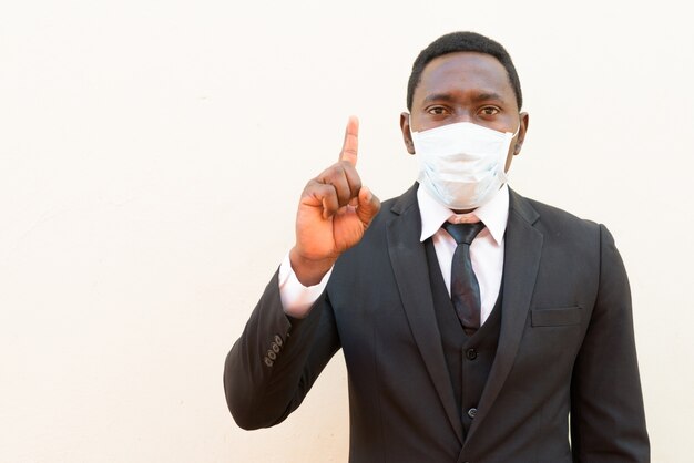 Homme d'affaires africain avec masque pointant vers le haut sur fond blanc