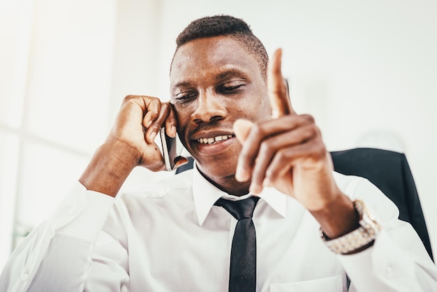 Homme d'affaires africain pensif parlant sur smartphone dans un bureau moderne.