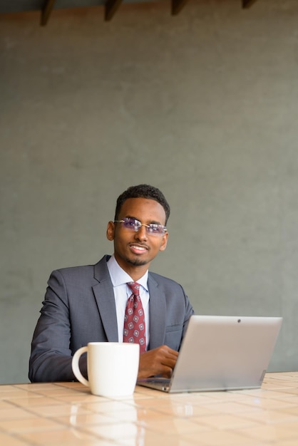 Homme d'affaires africain portant costume et cravate dans un café tout en utilisant un ordinateur portable