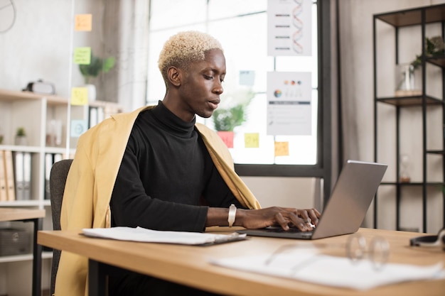 Homme d'affaires africain prospère en costume élégant travaillant sur un ordinateur portable sur un bureau moderne