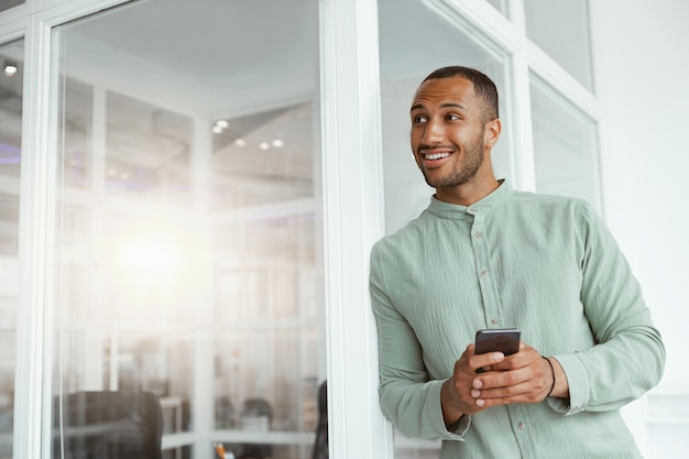 Homme d'affaires africain souriant debout dans un bureau moderne et tenant un téléphone