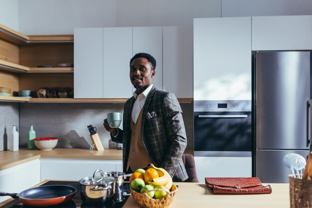 Homme d'affaires afro-américain allant travailler à la maison, prenant son petit déjeuner dans la cuisine, parlant au téléphone