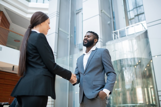Homme d'affaires afro-américain barbu en costume serrant la main d'un collègue tout en la félicitant avec succès du contrat