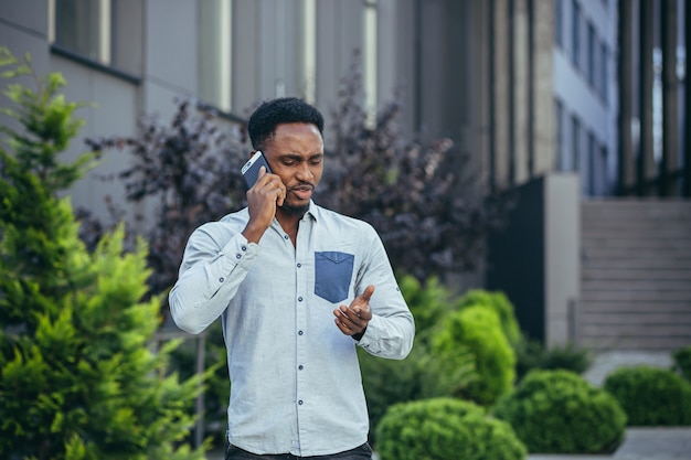 Homme d'affaires afro-américain en colère et sérieux parlant au téléphone se disputant marchant près de la maison