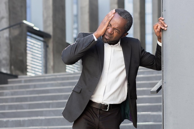 Homme d'affaires afro-américain en costume debout devant le bureau appuyé contre le mur qu'il tient