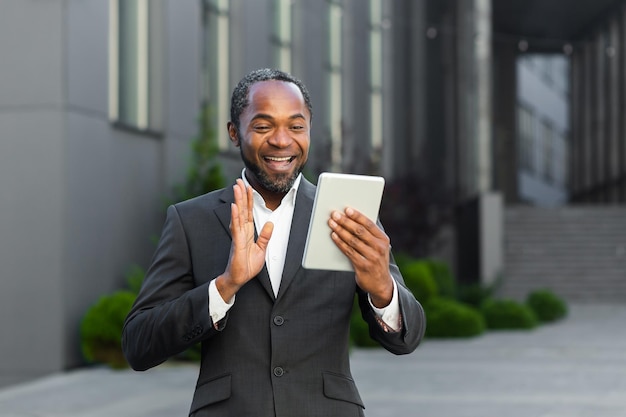 Un homme d'affaires afro-américain en costume se tient à l'extérieur d'un centre de bureau et parle lors d'un appel vidéo