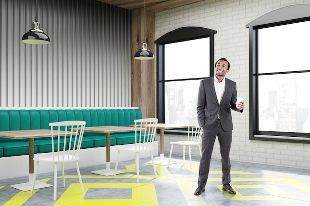 Homme d'affaires afro-américain debout dans un coin d'un intérieur de café avec un mur en bois gris, des tables carrées, des canapés verts et des chaises blanches près d'eux. rendu 3d, maquette