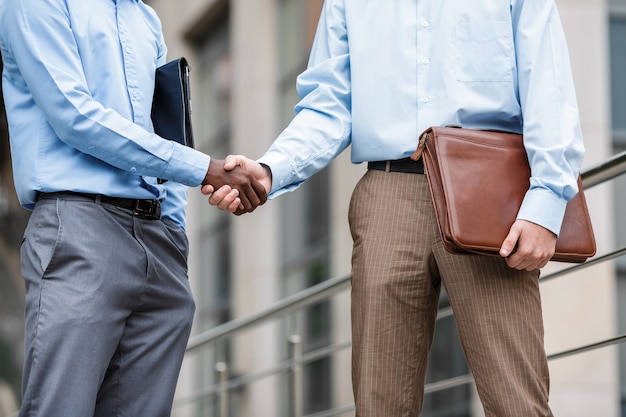 Homme d'affaires afro-américain et un homme d'affaires de race blanche se serrant la main sur les bâtiments, gros plan