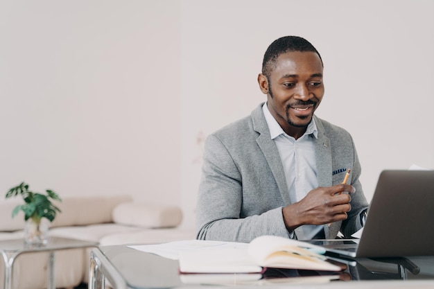 Homme d'affaires afro-américain lisant des e-mails avec de bonnes nouvelles sur un ordinateur portable au bureau souriant