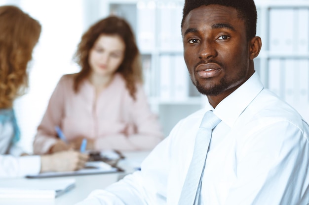 Homme d'affaires afro-américain lors d'une réunion au bureau, coloré en blanc. Groupe multiethnique de gens d'affaires.