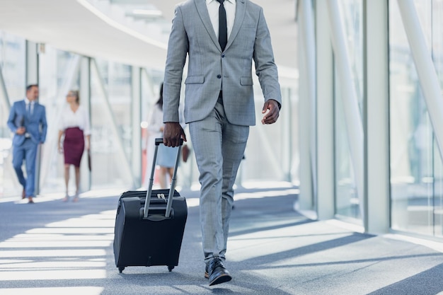 Un homme d'affaires afro-américain se promène dans le couloir avec une valise dans un bureau moderne.