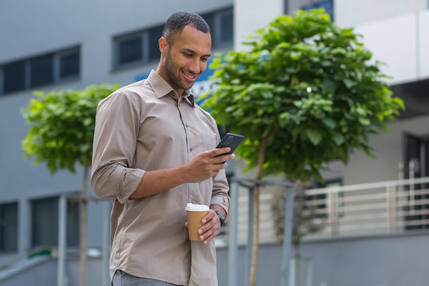 Homme d'affaires afro-américain souriant et heureux marchant à l'extérieur de l'immeuble de bureaux tenant une tasse de