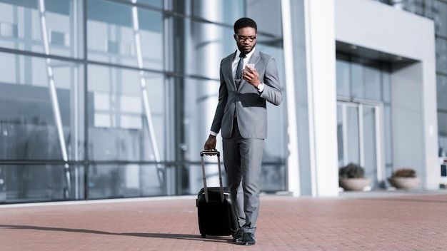 Homme d'affaires afro utilisant le téléphone arrivant à l'aéroport