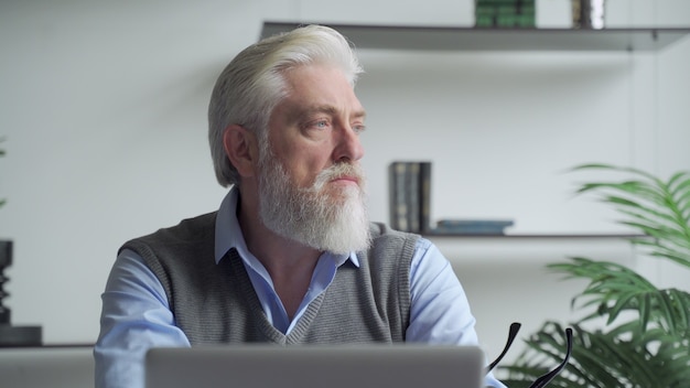 Un homme d'affaires âgé avec une barbe grise pensant à la solution du problème travaillant sur un ordinateur portable