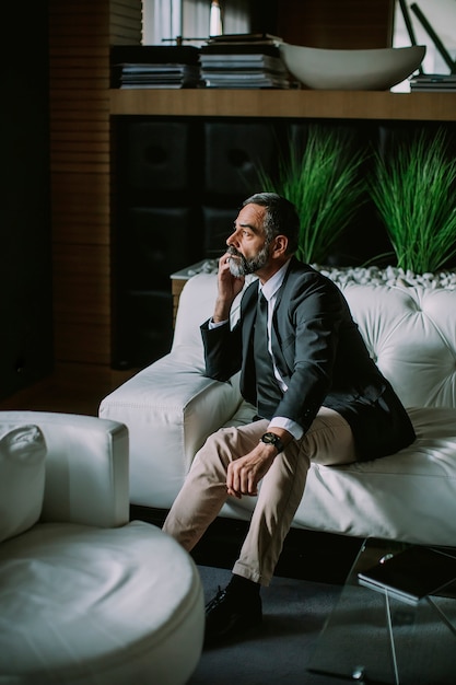 Photo homme d'affaires d'âge moyen à l'aide de téléphone portable dans un bureau moderne sur un canapé