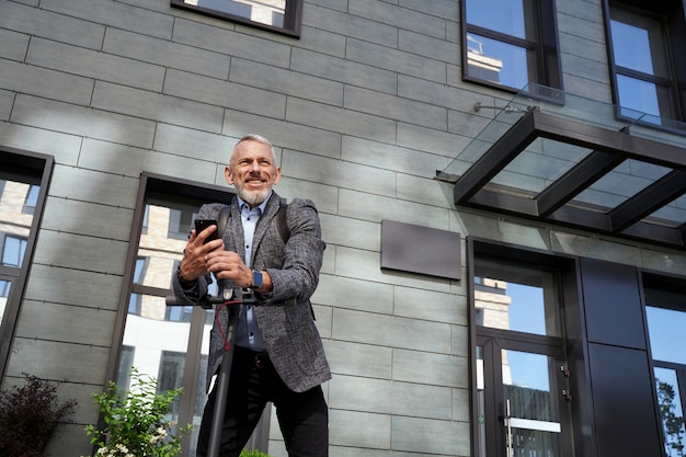 Homme d'affaires d'âge moyen confiant souriant tenant son téléphone portable en se tenant debout avec de l'électricité