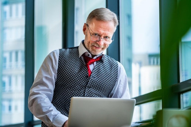 Homme d'affaires d'âge moyen en costume Assis avec un ordinateur portable près de la fenêtre Homme travaillant avec des documents Concept d'entreprise