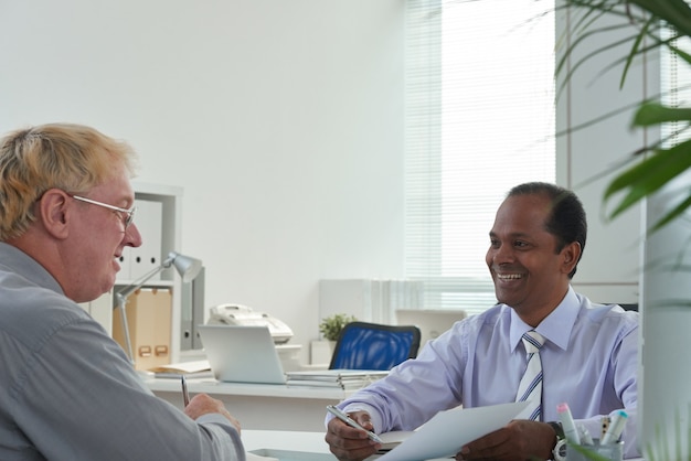Homme d'affaires d'âge moyen positif montrant un rapport avec des données financières à un collègue lors d'une réunion