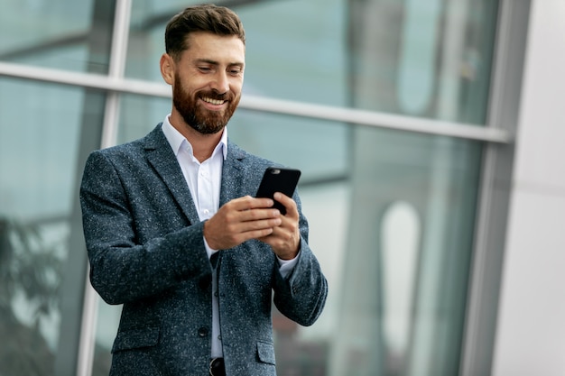 Homme d'affaires à l'aide de smartphone et souriant à l'aéroport. Jeune dirigeant d'entreprise avec téléphone portable à l'aéroport.