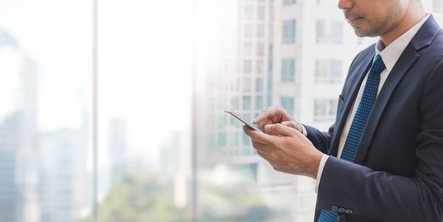 Homme d&#39;affaires à l&#39;aide de téléphone intelligent sur la fenêtre avec fond de bâtiment de la ville et de l&#39;espace de copie.