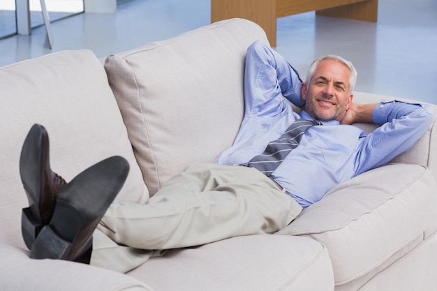 Homme d&#39;affaires allongé sur le canapé avec ses pieds en souriant à la caméra