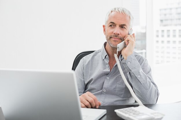 Homme d&#39;affaires sur appel en face de l&#39;ordinateur portable au bureau