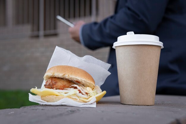 Homme d'affaires appréciant un sandwich et un café assis sur un banc près d'un immeuble de bureaux à l'extérieur de l'espace de copie Pause déjeuner