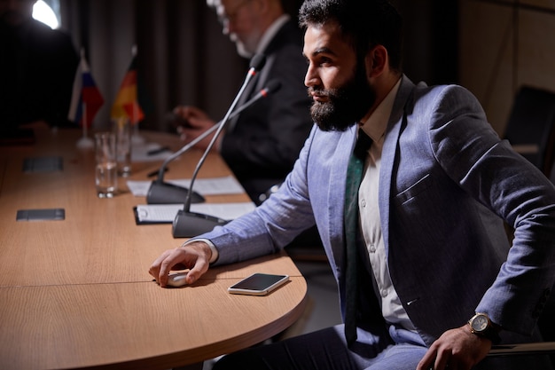 Homme D'affaires Arabe En Costume écoutant Attentivement L'un Des Rapport Des Orateurs, Assis Au Bureau Dans La Salle De Conférence, Lors D'une Réunion Sans Liens. Entreprise, Concept De Personnes Exécutives