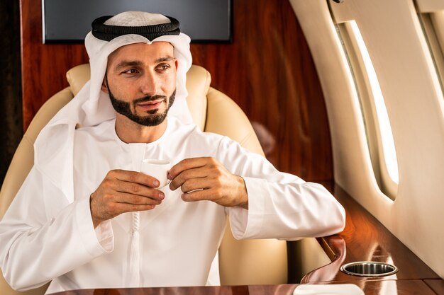 Homme d'affaires arabe avec costume traditionnel vole en classe affaires exclusive sur avion