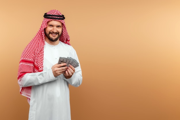 Un homme d'affaires arabe en tenue nationale tient des dollars dans ses mains.