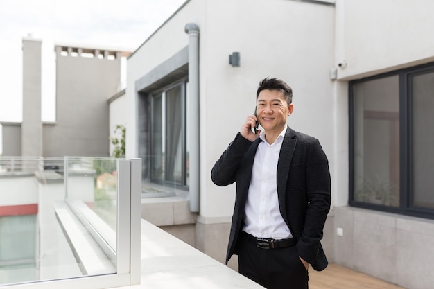 homme d'affaires asiatique en costume d'affaires bénéficie de la terrasse du téléphone permanent d'un centre de bureaux successfu