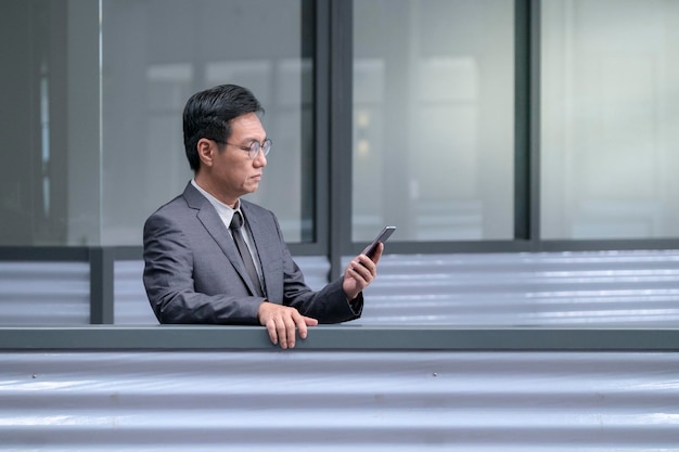 Homme d'affaires asiatique en costume et cravate lisant sur son téléphone portable