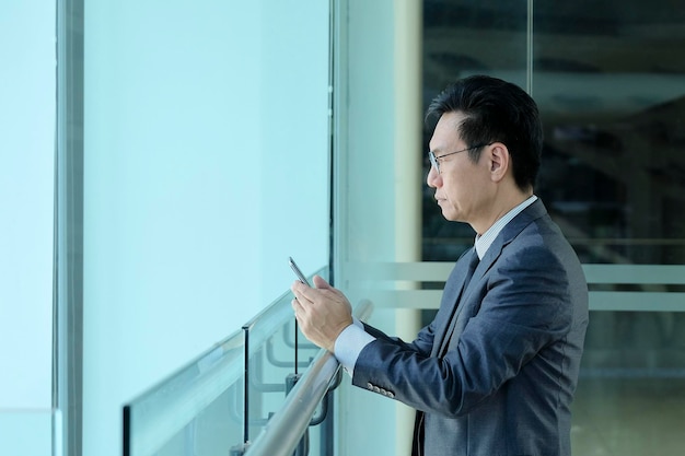 Homme d'affaires asiatique en costume debout avec les mains tenant son téléphone portable