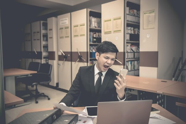 Un homme d'affaires asiatique en costume noir pense à une idée de travail au bureau, il fait des heures supplémentaires seul dans une entreprise