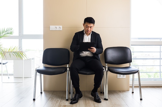 homme d'affaires asiatique dans la salle d'attente assis sur une chaise près de la réception du centre de bureaux