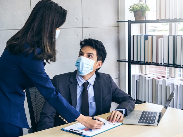 Homme d'affaires asiatique et femme portant un costume et des masques de protection regarder le tableau de rapport