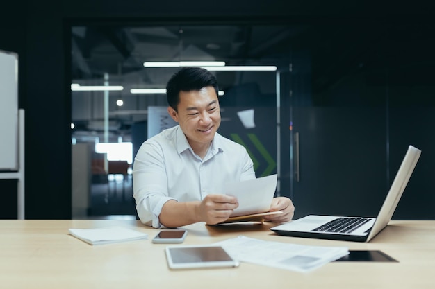 Homme d'affaires asiatique heureux et prospère lisant le patron de la lettre de document financier travaillant avec des documents