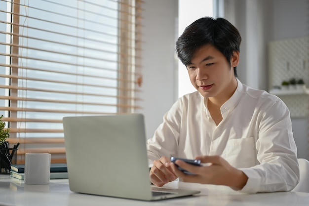 Homme d'affaires asiatique inspiré regardant l'écran de son ordinateur portable travaillant sur son projet d'entreprise