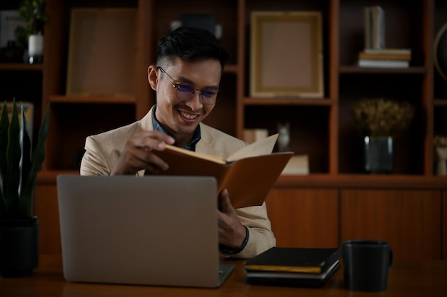 Homme d'affaires asiatique intelligent lisant un livre à son bureau dans la salle de bureau