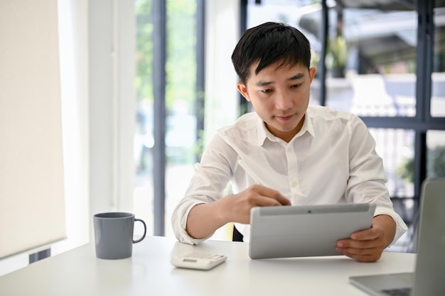 Homme d'affaires asiatique intelligent ou patron masculin utilisant sa tablette et travaillant au bureau