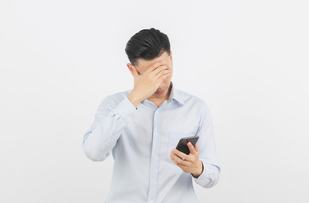 Homme d'affaires asiatique jeune mécontent et frustré par quelque chose sur smartphone. Expression faciale négative isolée sur blanc