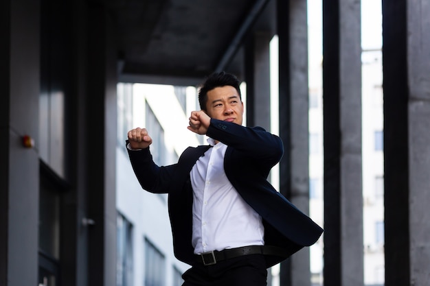 Un homme d'affaires asiatique joyeux et joyeux dansant près du bureau se réjouit de la victoire et du succès