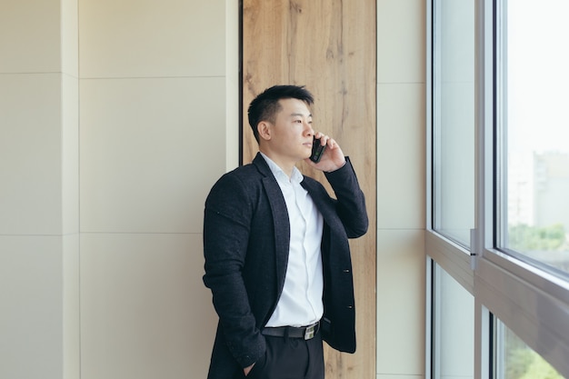 Un homme d'affaires asiatique parlant au téléphone dans un centre de bureaux moderne passe un appel de travail à ses collègues