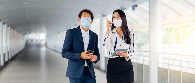 Homme d'affaires asiatique parlant au téléphone portable et belle jeune femme travaillant sur une tablette numérique debout à l'extérieur de l'immeuble de bureaux.