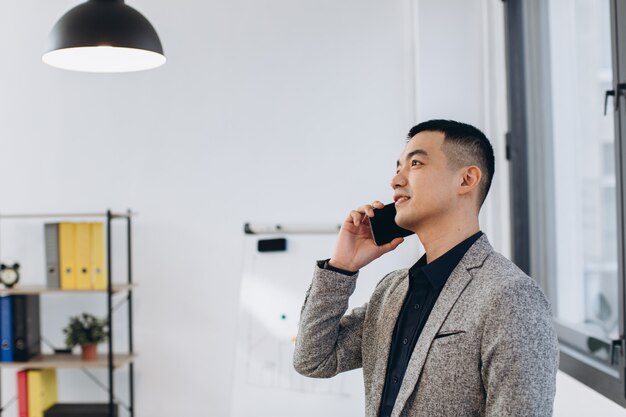 Homme d'affaires asiatique parlant sur téléphone mobile dans le bureau loft moderne