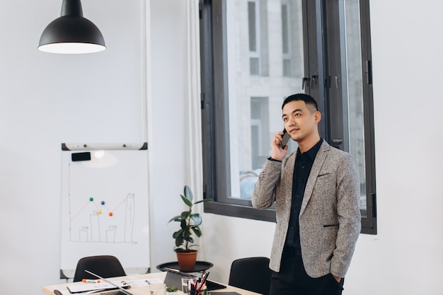 Homme d'affaires asiatique parlant sur téléphone mobile dans le bureau loft moderne